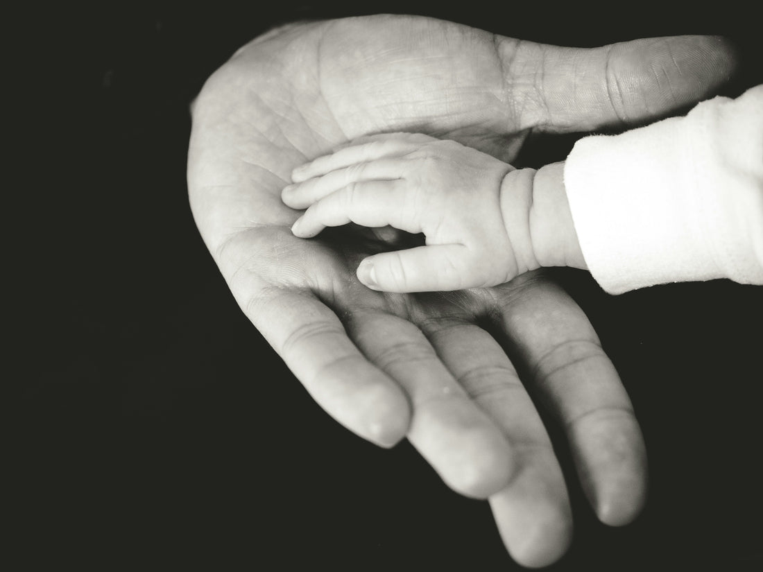 A baby's hand resting in a father's hand, black and white photo by Liane Metzler on Unsplash