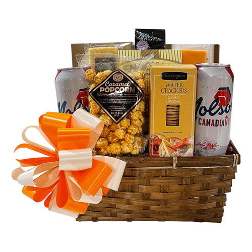 Woven gift basket with caramel popcorn, water crackers, assorted snacks, two cans of Canadian beer, and an orange and white decorative bow.