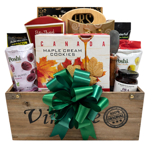 Wooden gift basket filled with Canadian maple cream cookies, assorted gourmet snacks including olives, chocolates, and preserves, adorned with a large green bow.