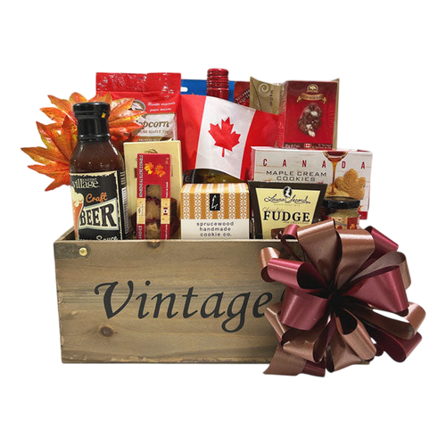 Wooden gift basket labeled Vintage filled with Canadiana Wine bottle, Canadian flag, fudge, maple cream cookies, popcorn, sauce, and other gourmet treats, adorned with brown ribbon bow.